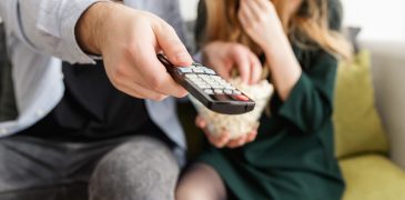 couple on couch with popcorn about to watch television 4 Reasons TV Should Still Be in Your Media Plan