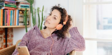 Woman sitting inside thoughtfully listening to audio via headphones