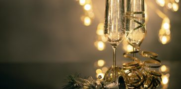 Close up of two filled champaign glasses with lights in the background