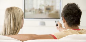 back of couple sitting on couch watching television