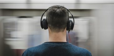 Man wearing headphones while train passes.